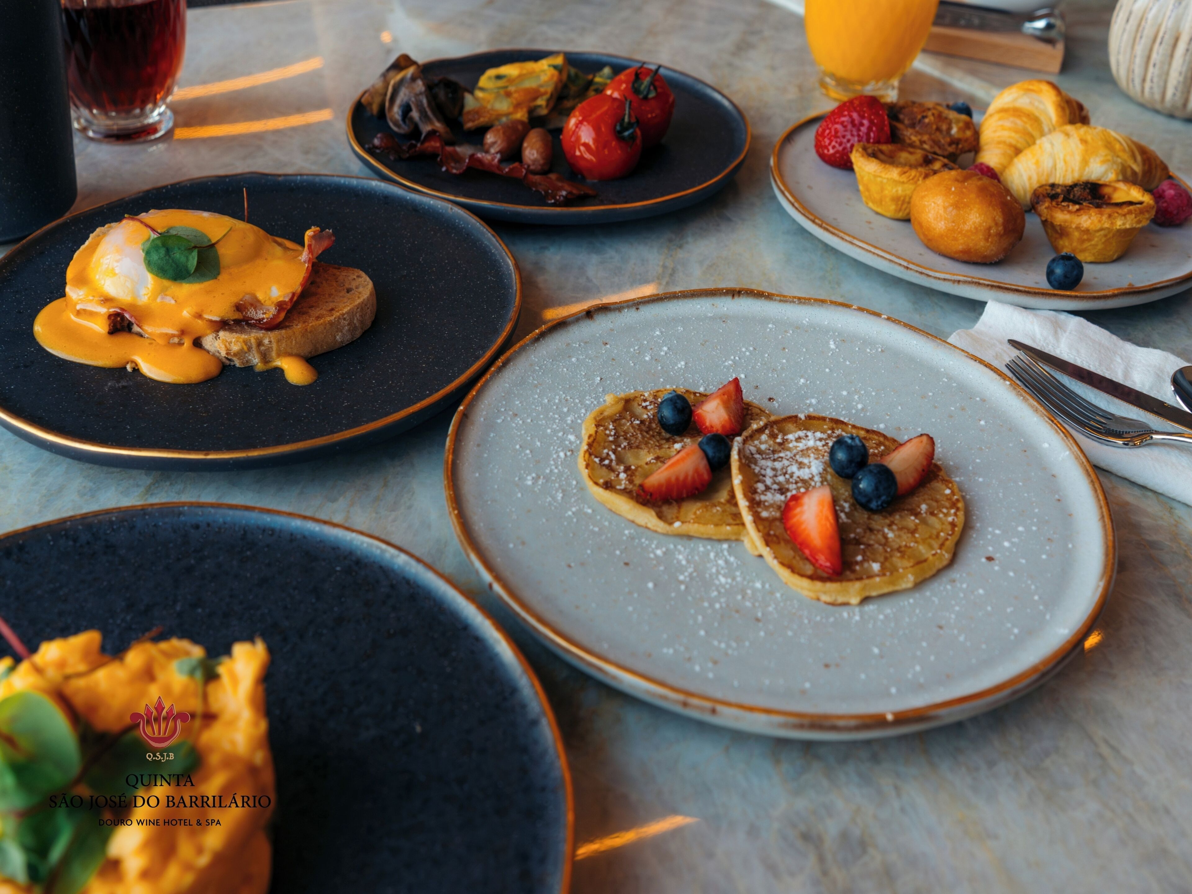 A breakfast setting with various dishes including pancakes, eggs, and pastries on plates.