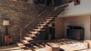 A spacious living area with a wooden staircase, a brick wall, and a wooden floor.