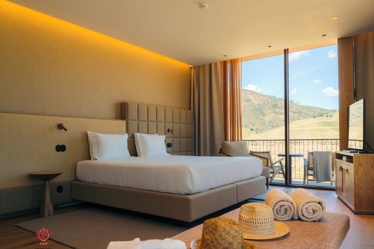 Ett hotellrum med en stor säng, en TV, en balkong med utsikt över landskapet och en minibar.