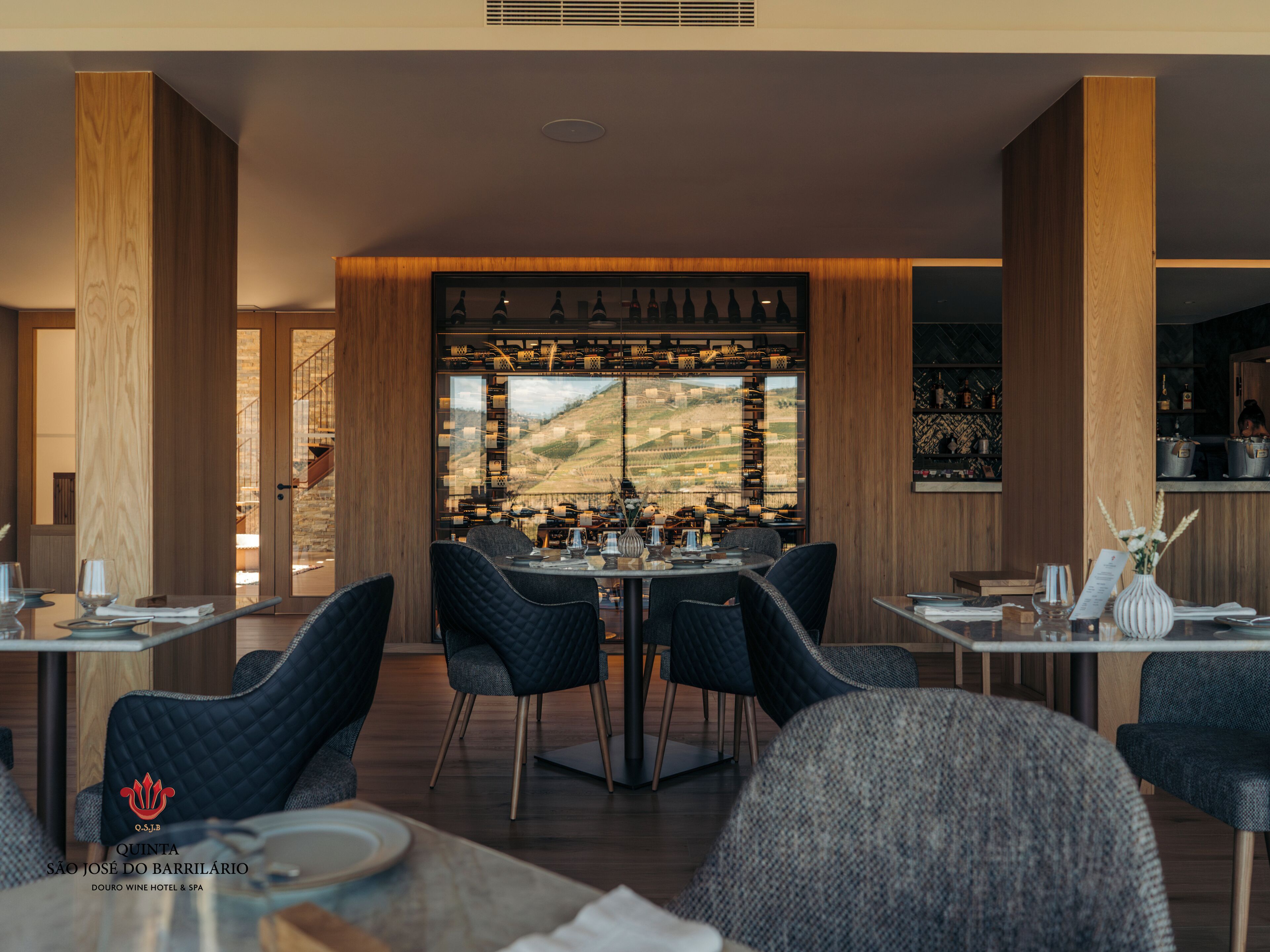 A restaurant with a view of vineyards, wooden paneling, and a wine rack with bottles.