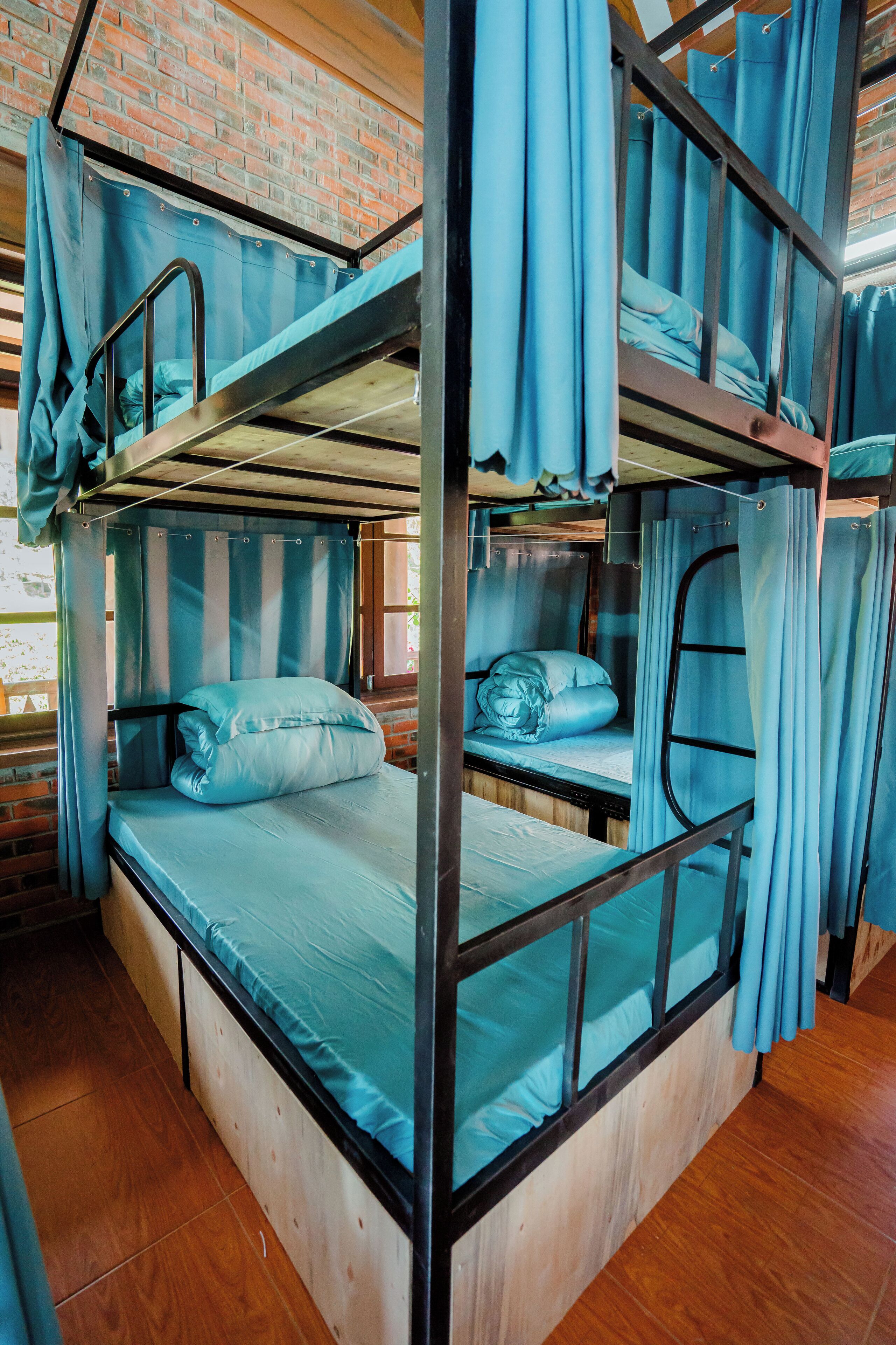 A bunk bed room with curtains, wooden flooring, and a brick wall.