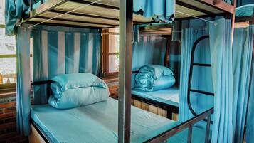 A bunk bed room with curtains, wooden flooring, and a brick wall.