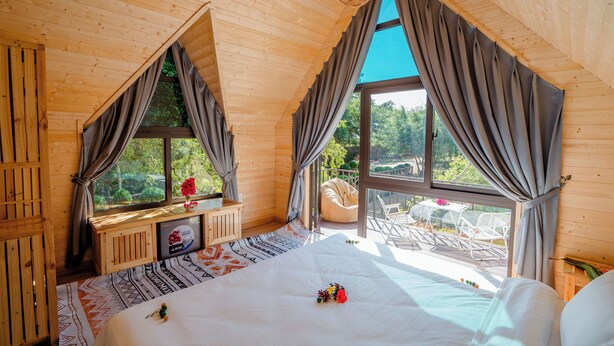 A wooden cabin bedroom with a large bed, a window seat with a table, and a view of the outdoors.