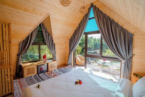 A wooden cabin bedroom with a large bed, a window seat with a table, and a view of the outdoors. - Bai Tu Long Mountain Resort (Van Don)