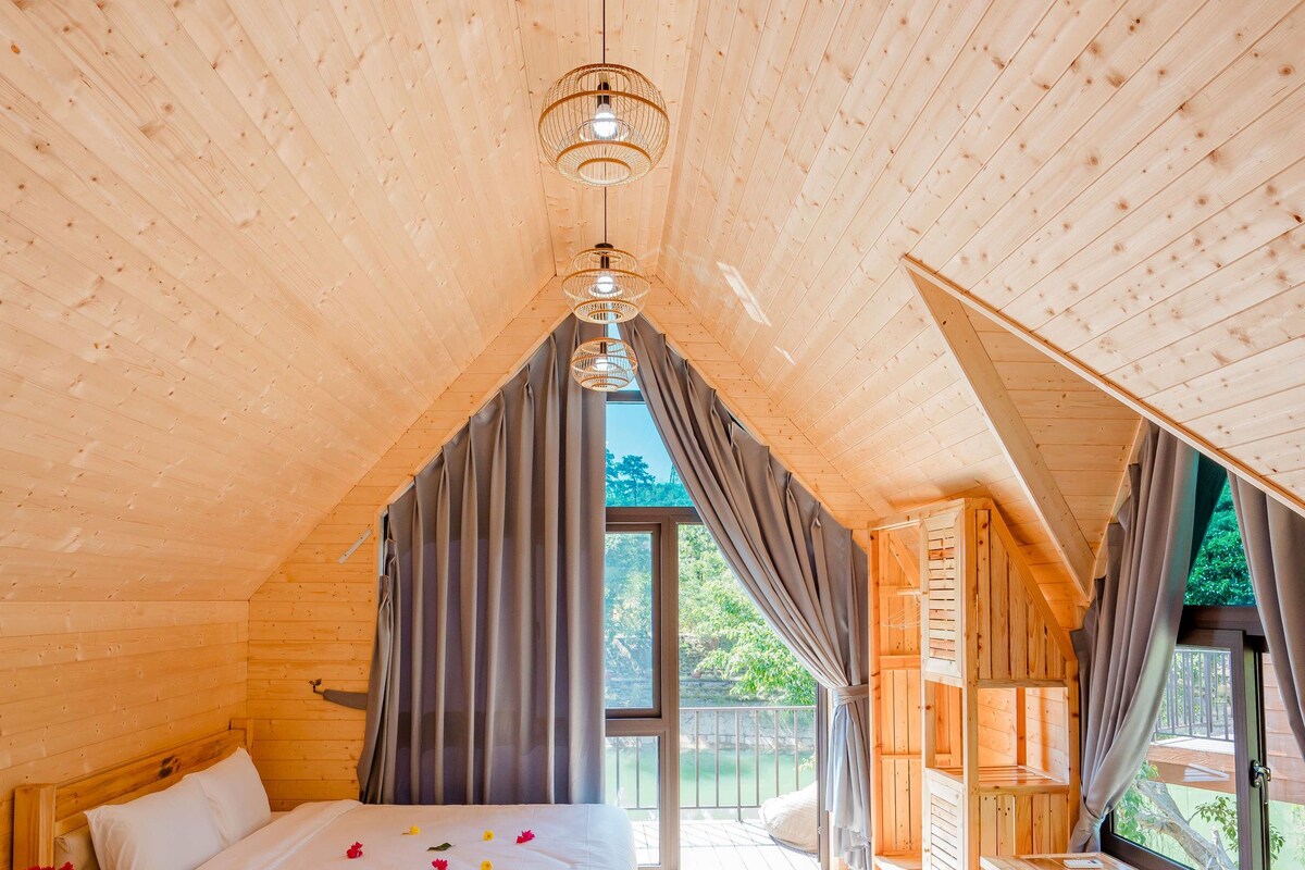 A wooden cabin bedroom with two beds, a dining area, and a view of the outdoors.