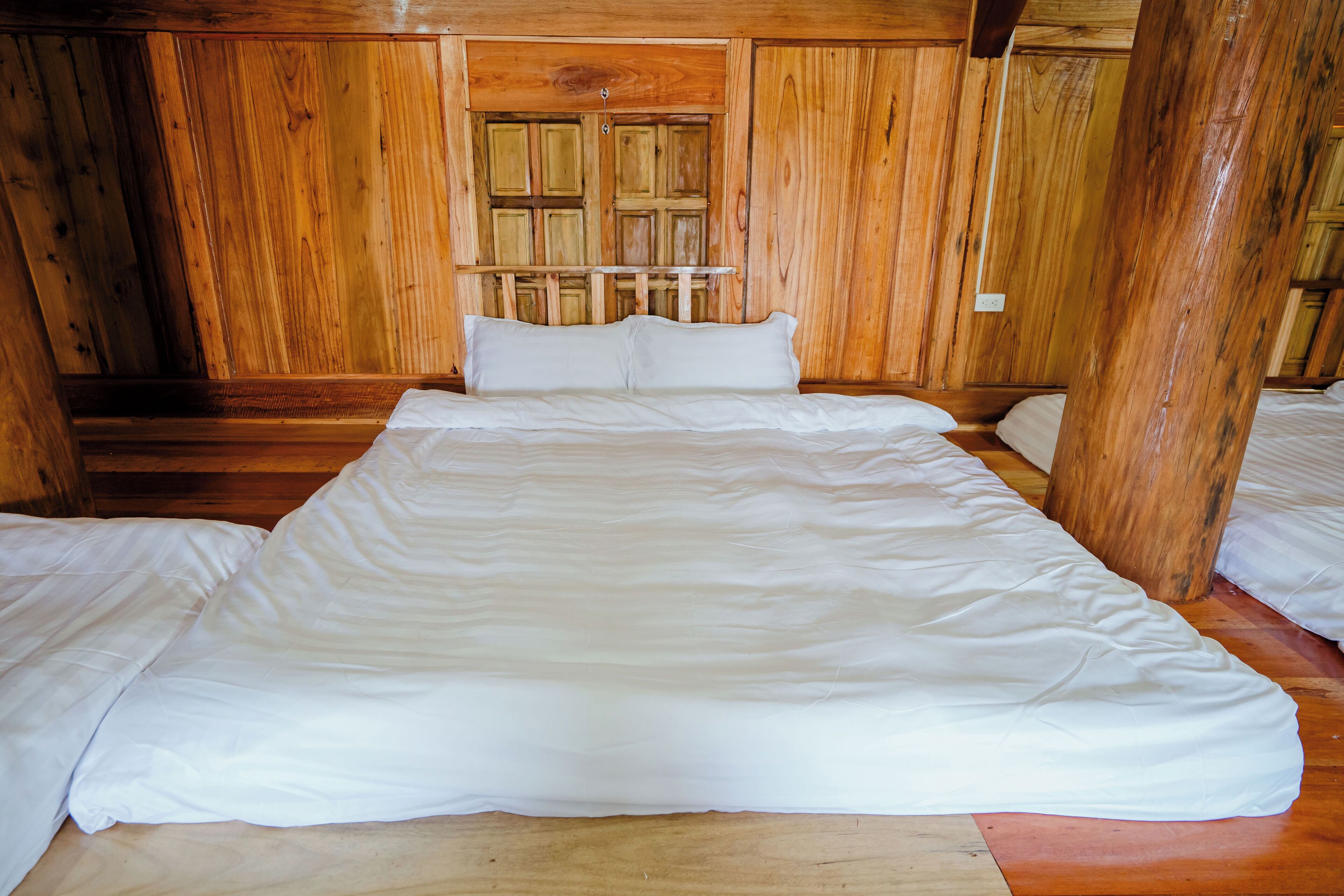 A wooden-paneled room with a large bed, a small table, and a window with wooden shutters.