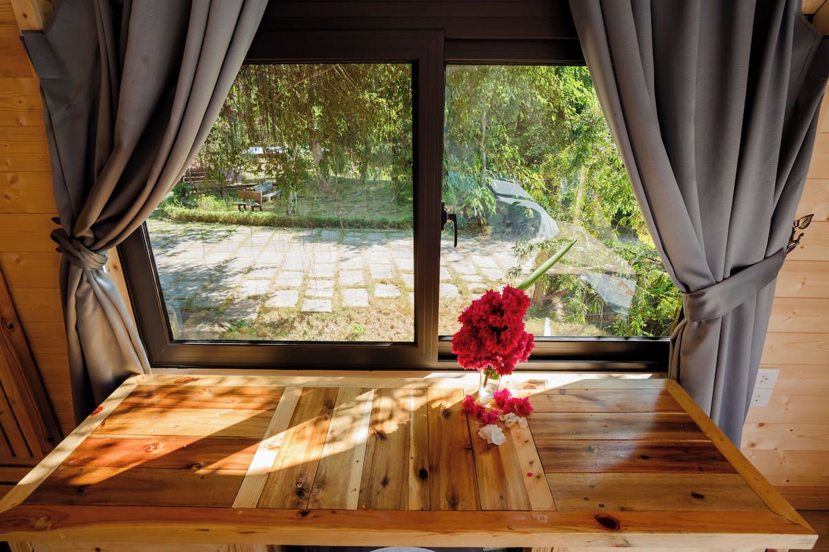 Un tavolo in legno con un vaso di fiori davanti a una finestra con tende.