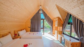 A wooden cabin with two beds, a small table, and a window with curtains.