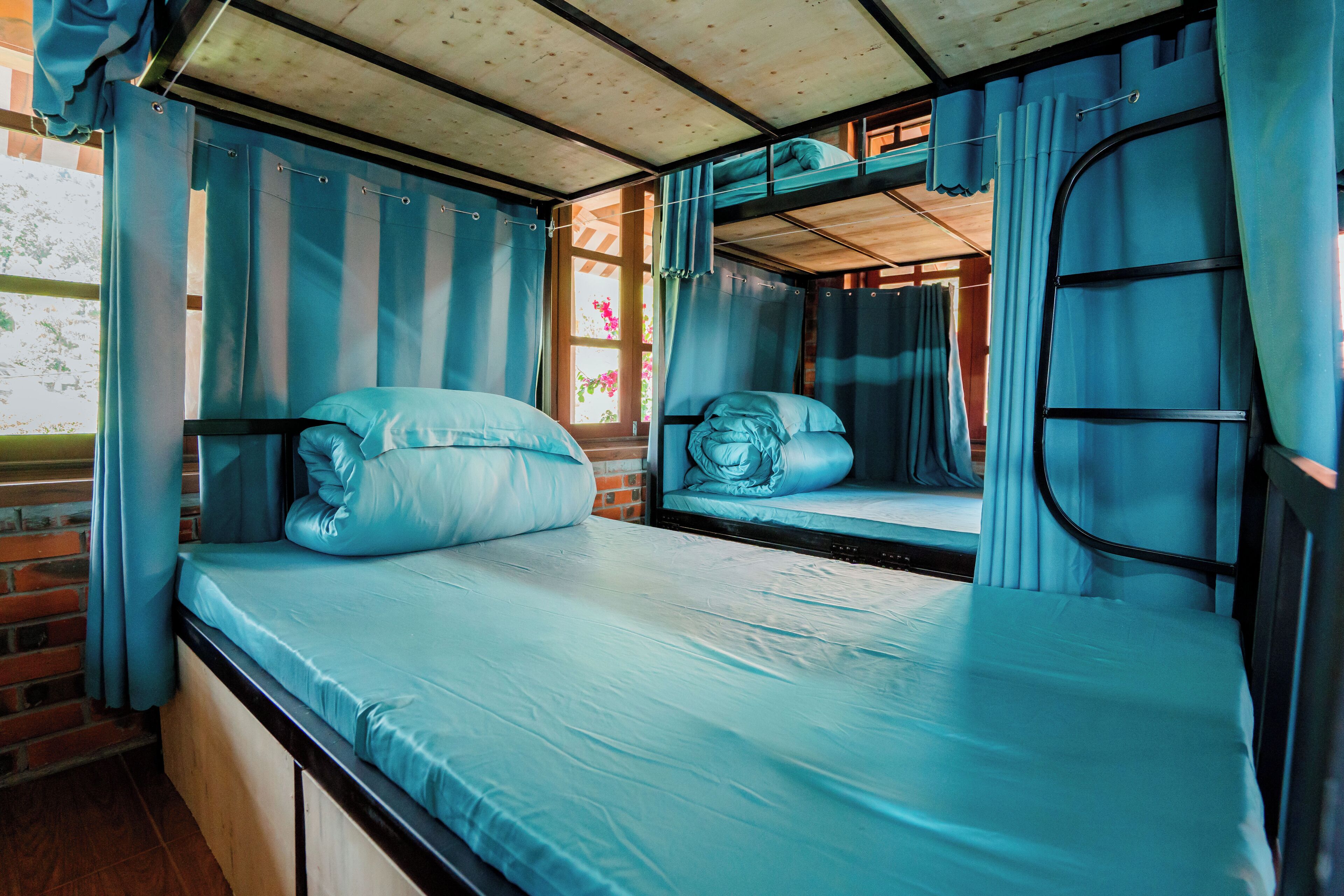 A train compartment with two beds, each with a pillow and a blanket, and a window with curtains.