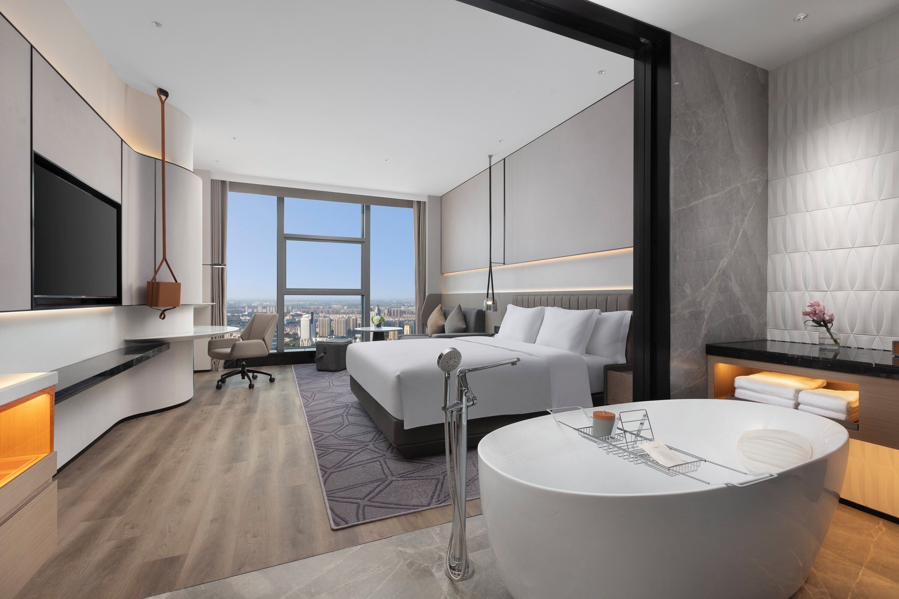 Une chambre d’hôtel moderne dotée d’un grand lit, d’un coin salon, d’une baignoire et offrant une vue sur la ville.