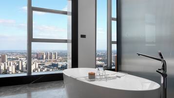 A modern bathroom with a freestanding bathtub, a large window offering a city view, and a frosted glass door.