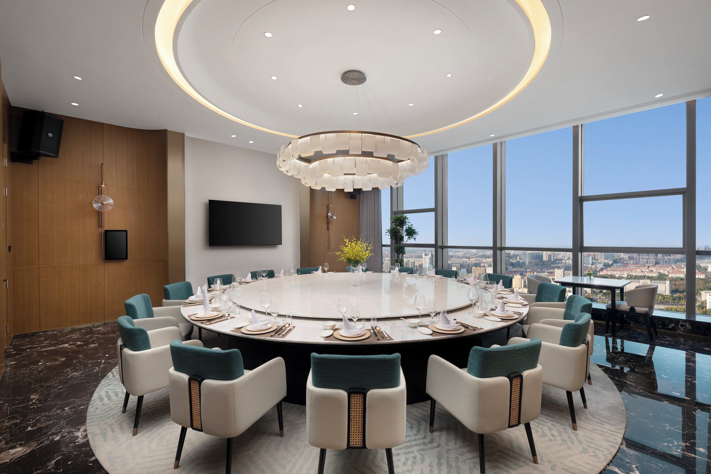 Un salón de conferencias con una mesa redonda, sillas, una araña y una televisión, con vista a la ciudad.