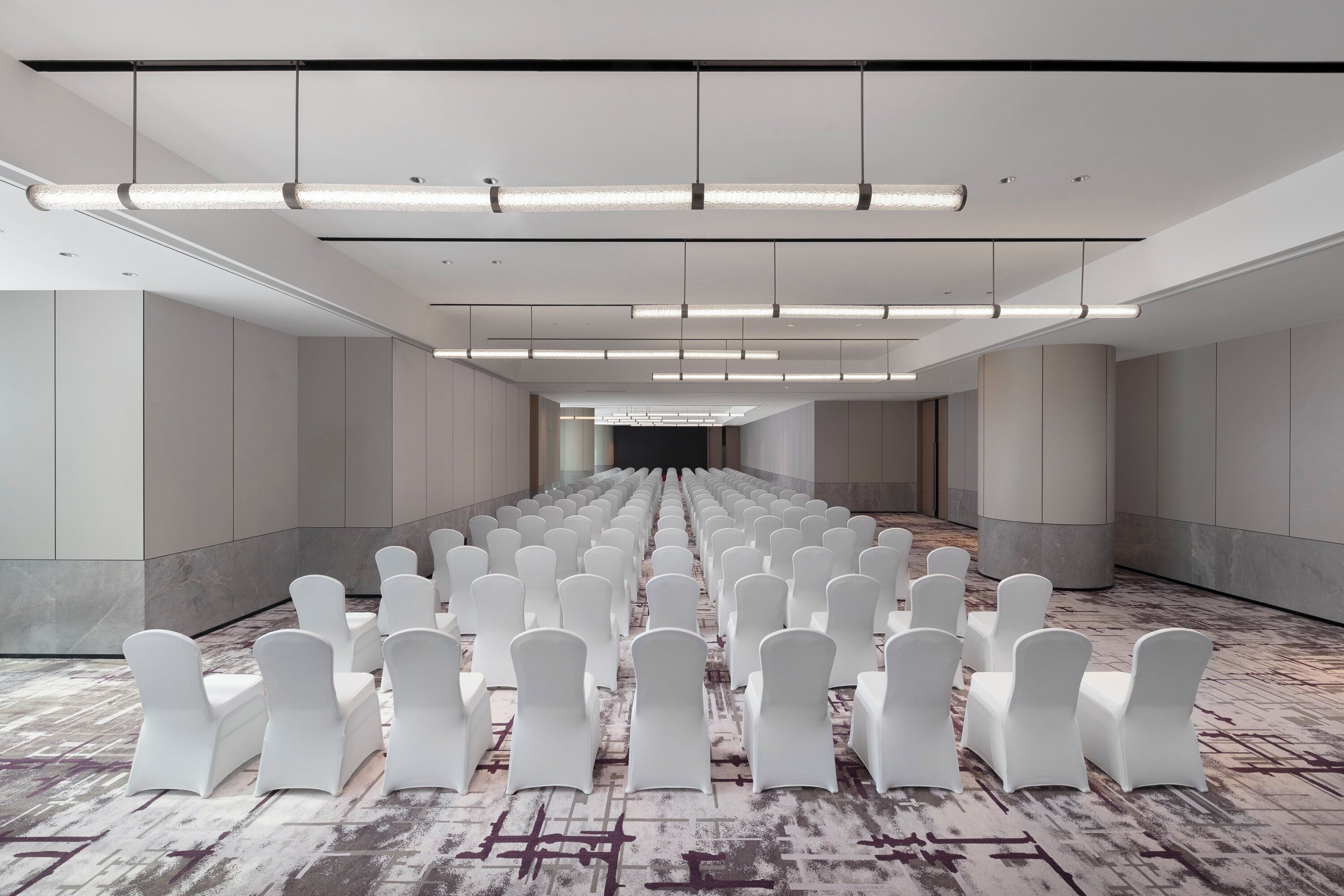 A spacious hall with rows of white chairs and overhead lighting.
