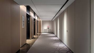 Un pasillo moderno de hotel con una alfombra de diseño geométrico, un mostrador de recepción y una señal en la pared que indica la habitación número 38.