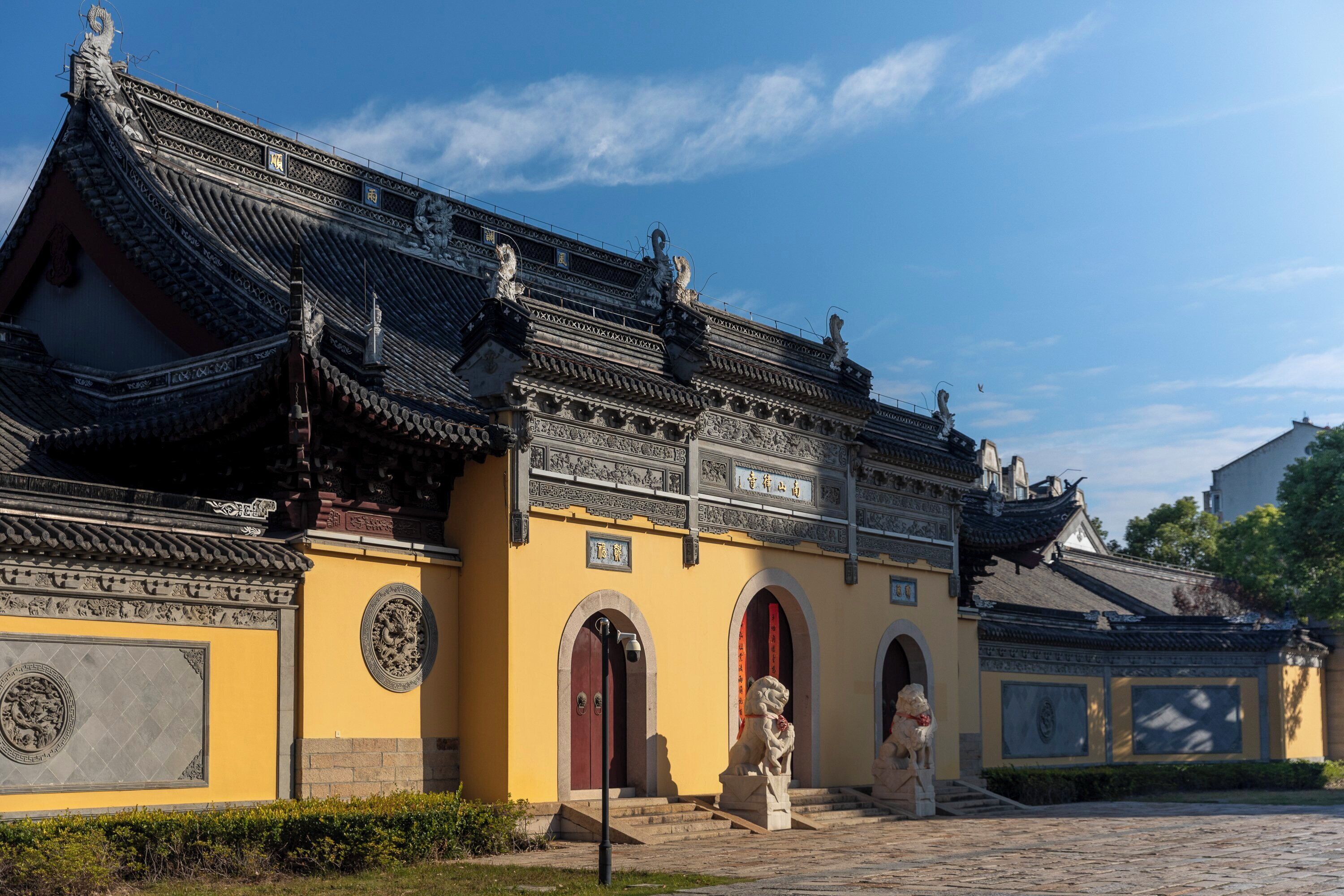 A traditional building with ornate roof tiles, a yellow facade, and two lion statues at the entrance.