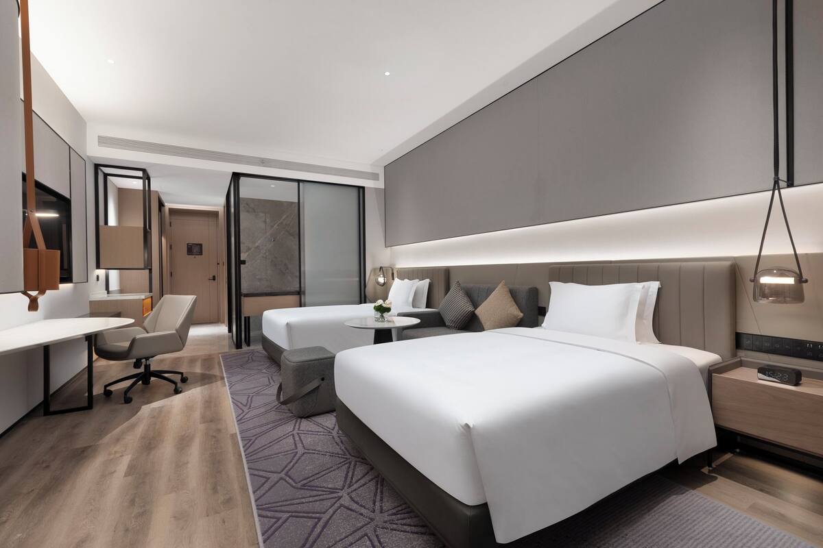 A modern hotel room with a large bed, a desk, a chair, and a small table.