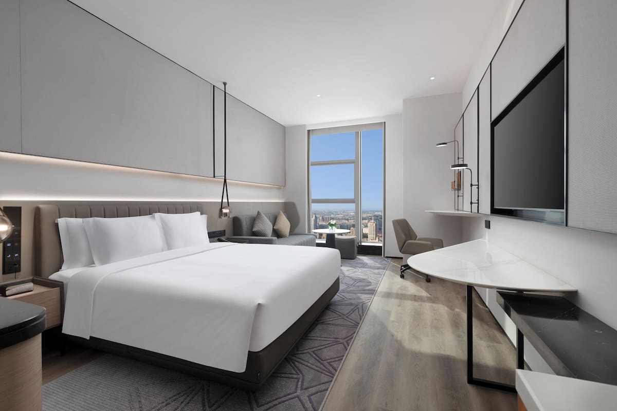 A modern hotel room with a large bed, a desk, a chair, and a TV.