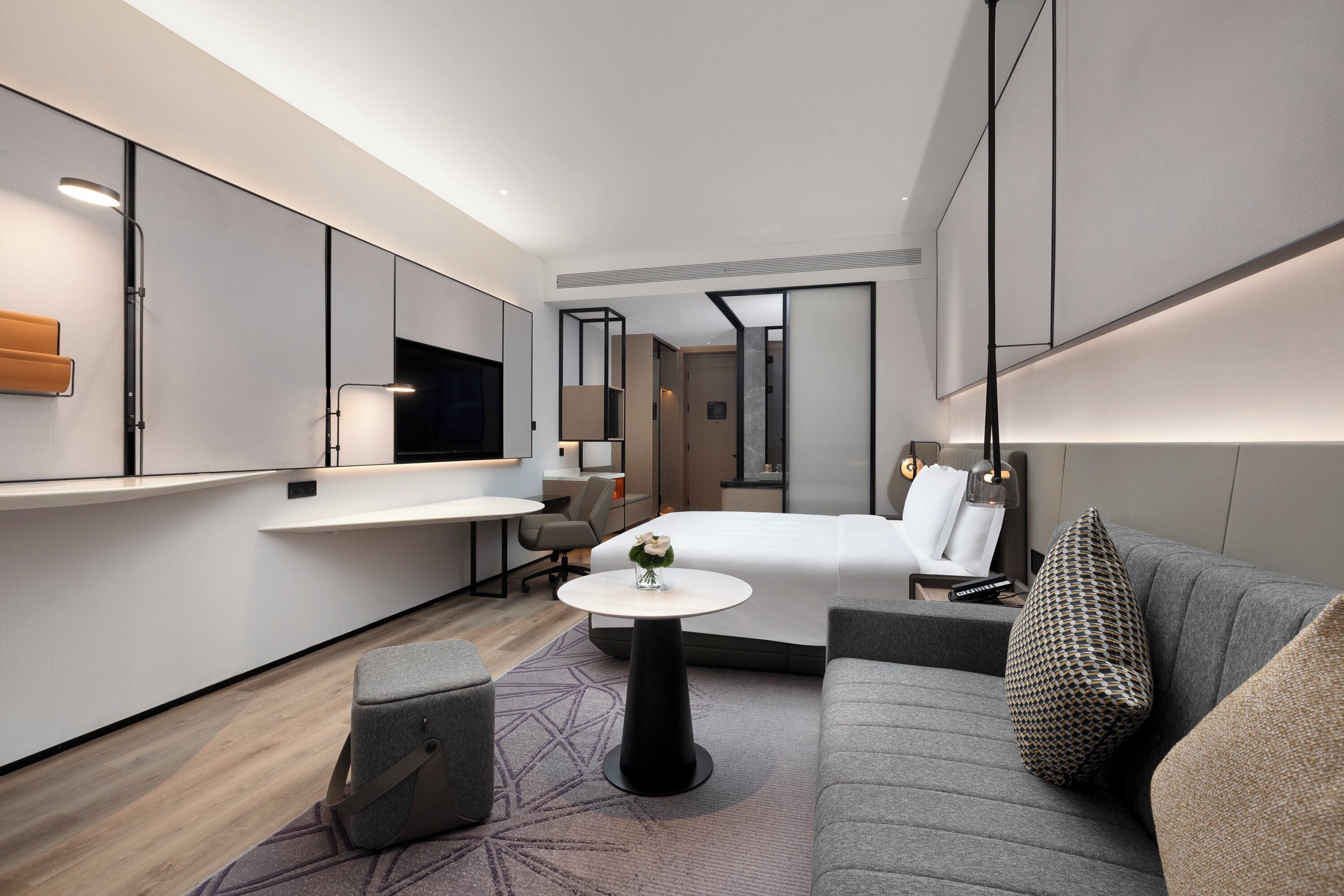 Una habitación de hotel moderna con cama, sofá, una mesita y un espejo.