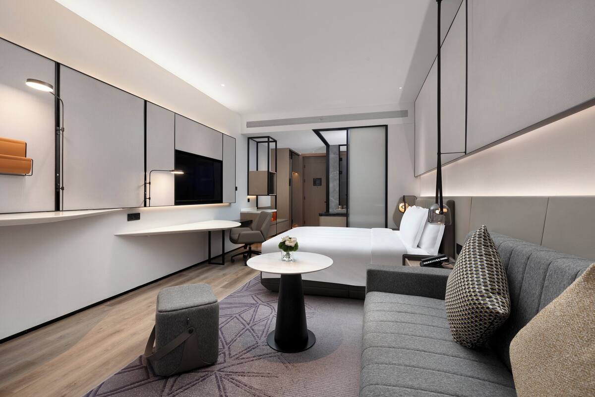 A modern hotel room with a bed, a sofa, a small table, and a mirror.