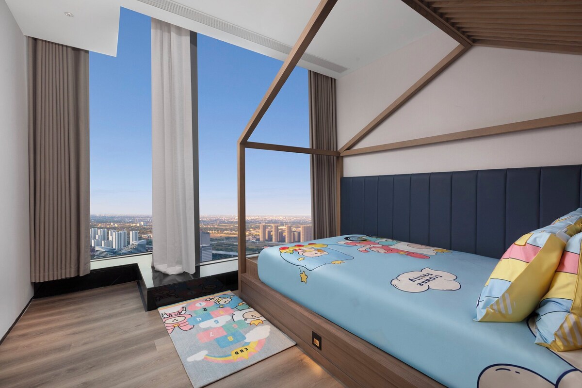 A modern bedroom with a city view, a bed with cartoon-themed bedding, and a wooden floor.