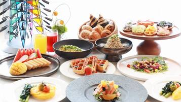 Una selezione di cibi per la colazione, tra cui waffle, pasticcini e frutta, su un tavolo.