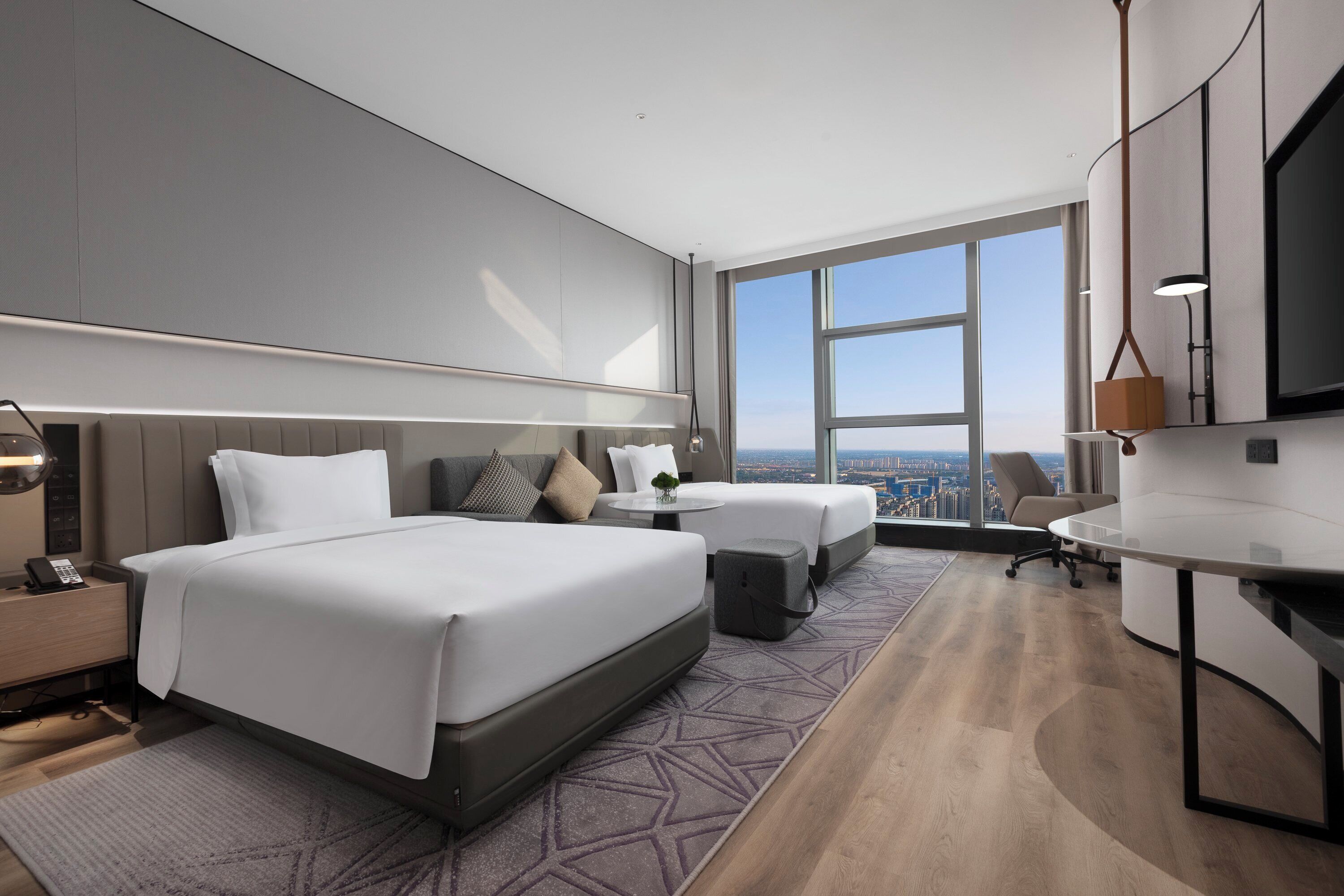 A modern hotel room with a large bed, a desk, and a view of the city.