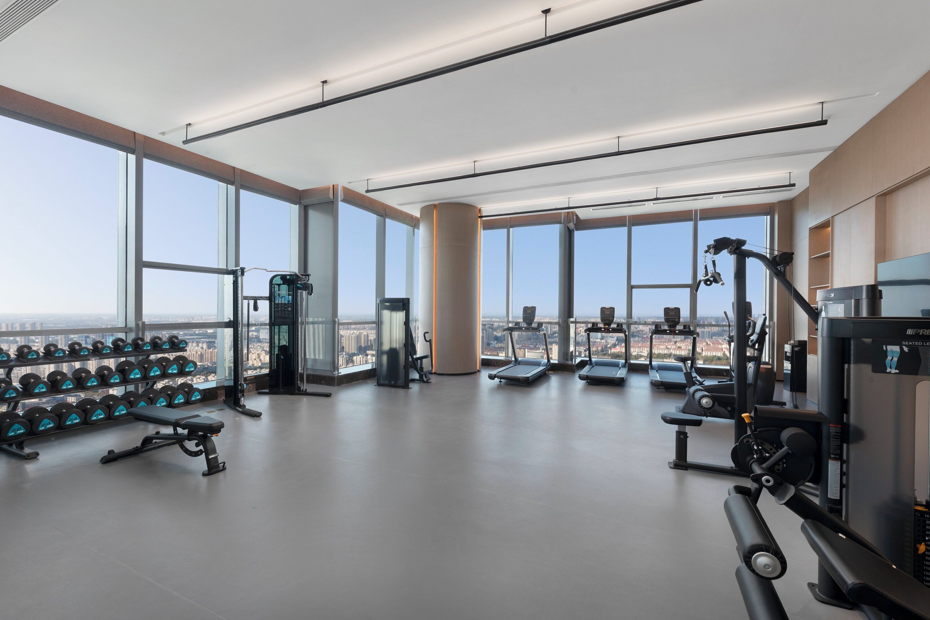 A modern gym with large windows, various exercise equipment, and a bench.