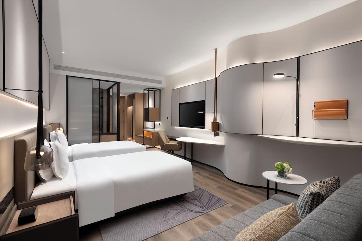 A modern hotel room with a large bed, a sofa, a small table with a plant, and a TV mounted on the wall.