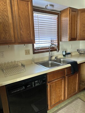 A kitchen with wooden cabinets, a dishwasher, a sink, and a window with blinds.