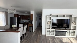 En moderne stue med et fladskærms-tv, et spiseområde med et træbord, og et køkken i baggrunden.