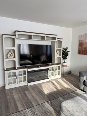A modern living room with a flat-screen TV, built-in shelving, and a potted plant.