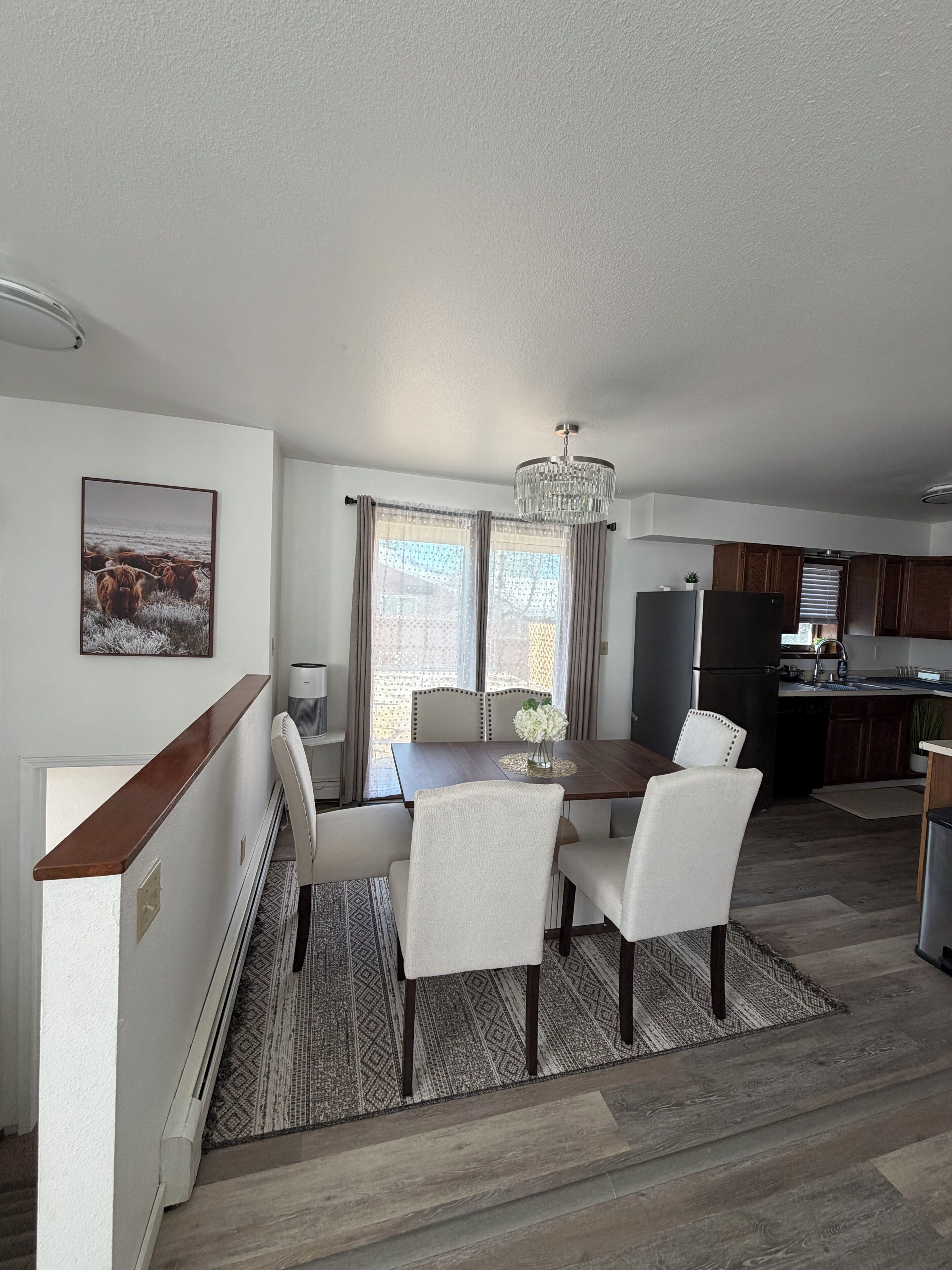 A modern kitchen with dark cabinetry, a central island, and a dining area with a table and chairs.