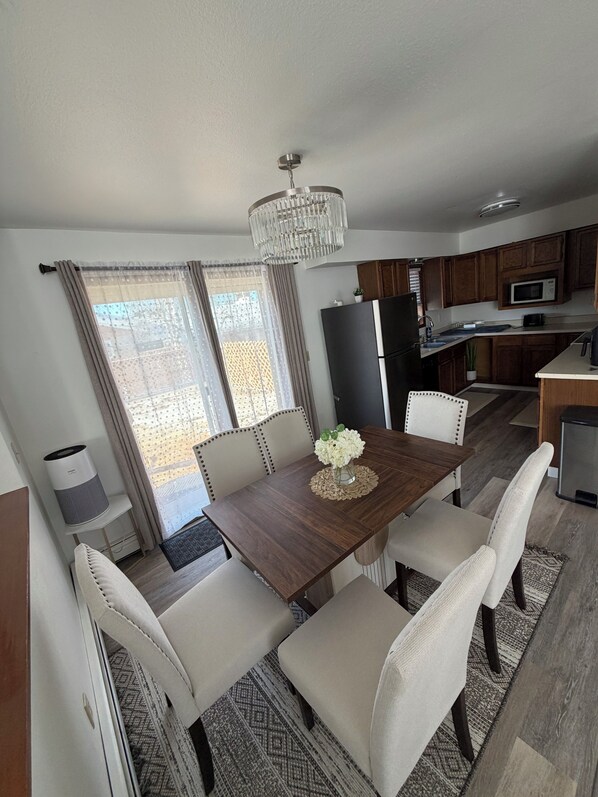 A modern kitchen with a central island, dining table with chairs, and a chandelier.