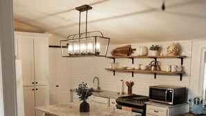 A kitchen with white cabinets, a granite countertop, a stainless steel stove, and a microwave. - The Cottage at Cardinal Hill (Dahlonega)