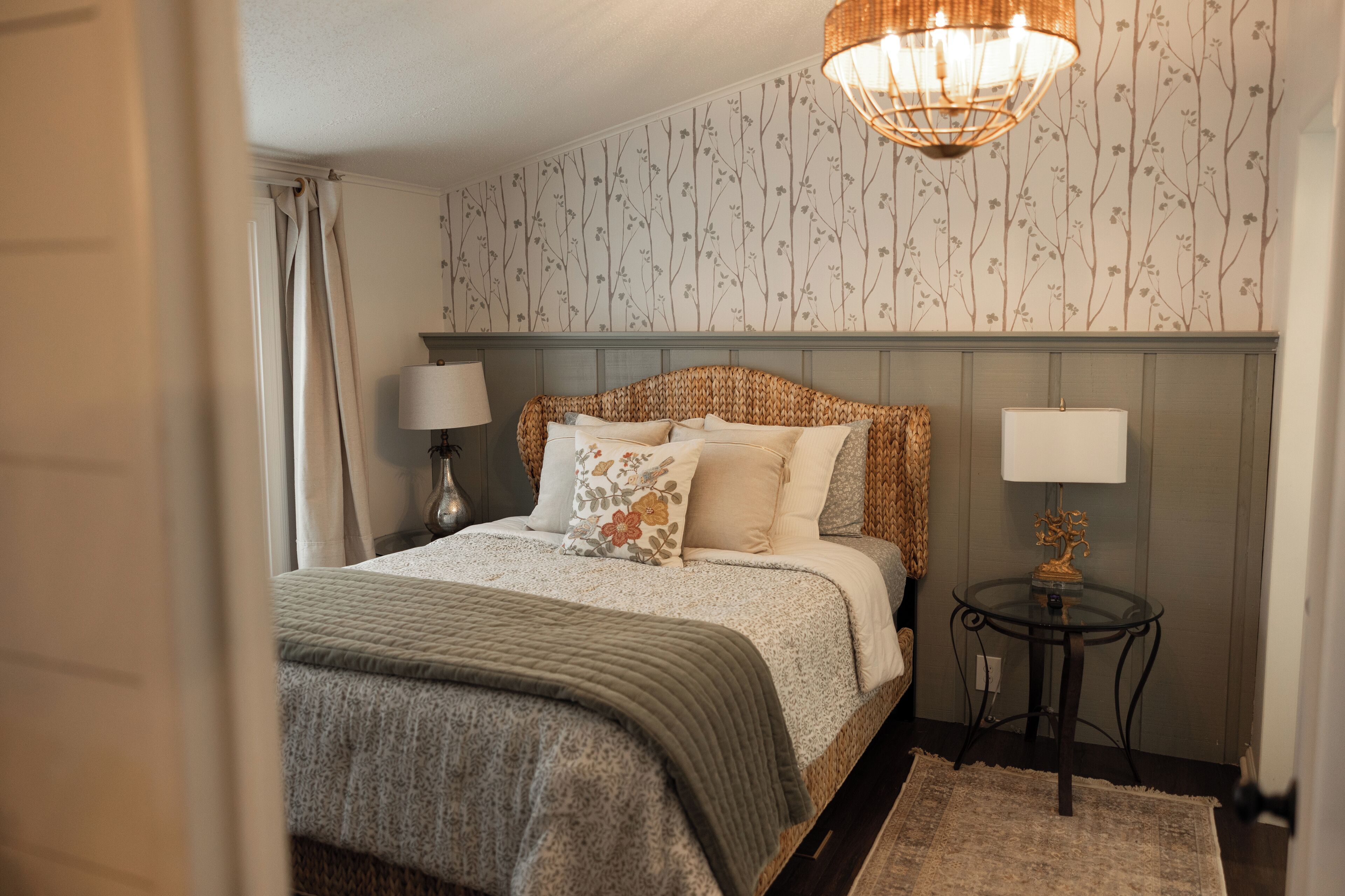 A bedroom with a bed, two bedside lamps, a round table with a lamp, and a patterned wallpaper.
