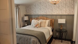 A bedroom with a bed, two bedside lamps, a round table with a lamp, and a patterned wallpaper. - The Cottage at Cardinal Hill (Dahlonega)