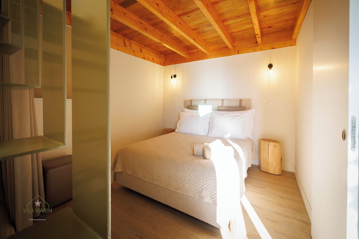 A bedroom with a wooden ceiling, a bed with white linens, and a small bedside table.