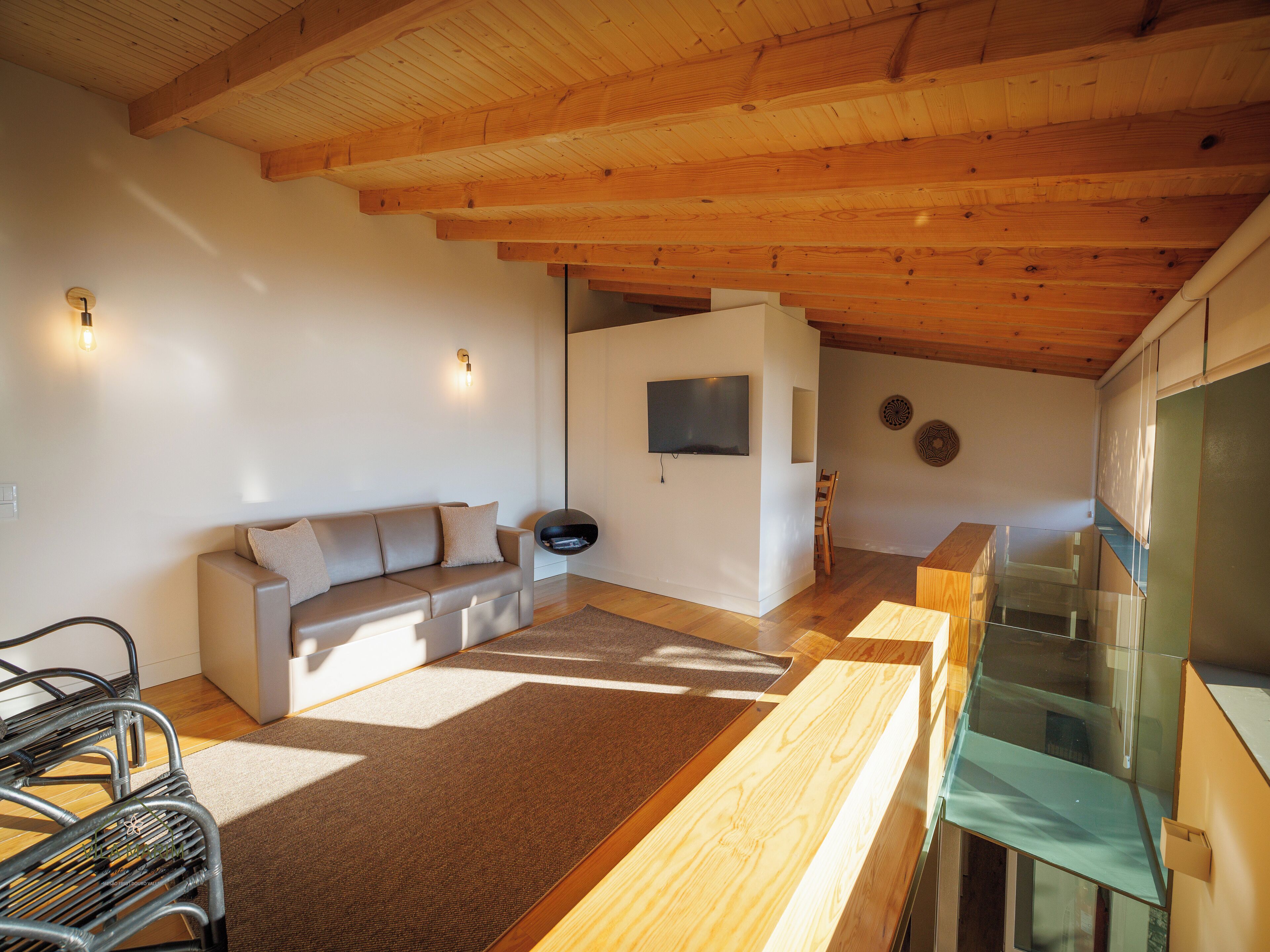 A modern living room with a wooden ceiling, a sofa, a TV, and a glass staircase.