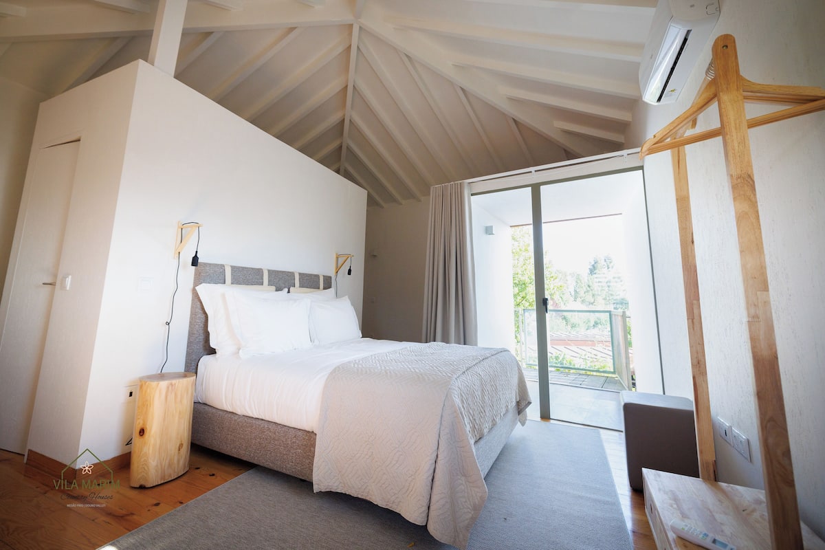A bedroom with a bed, a wooden bedside table, a hanging wooden rack, and a large window.