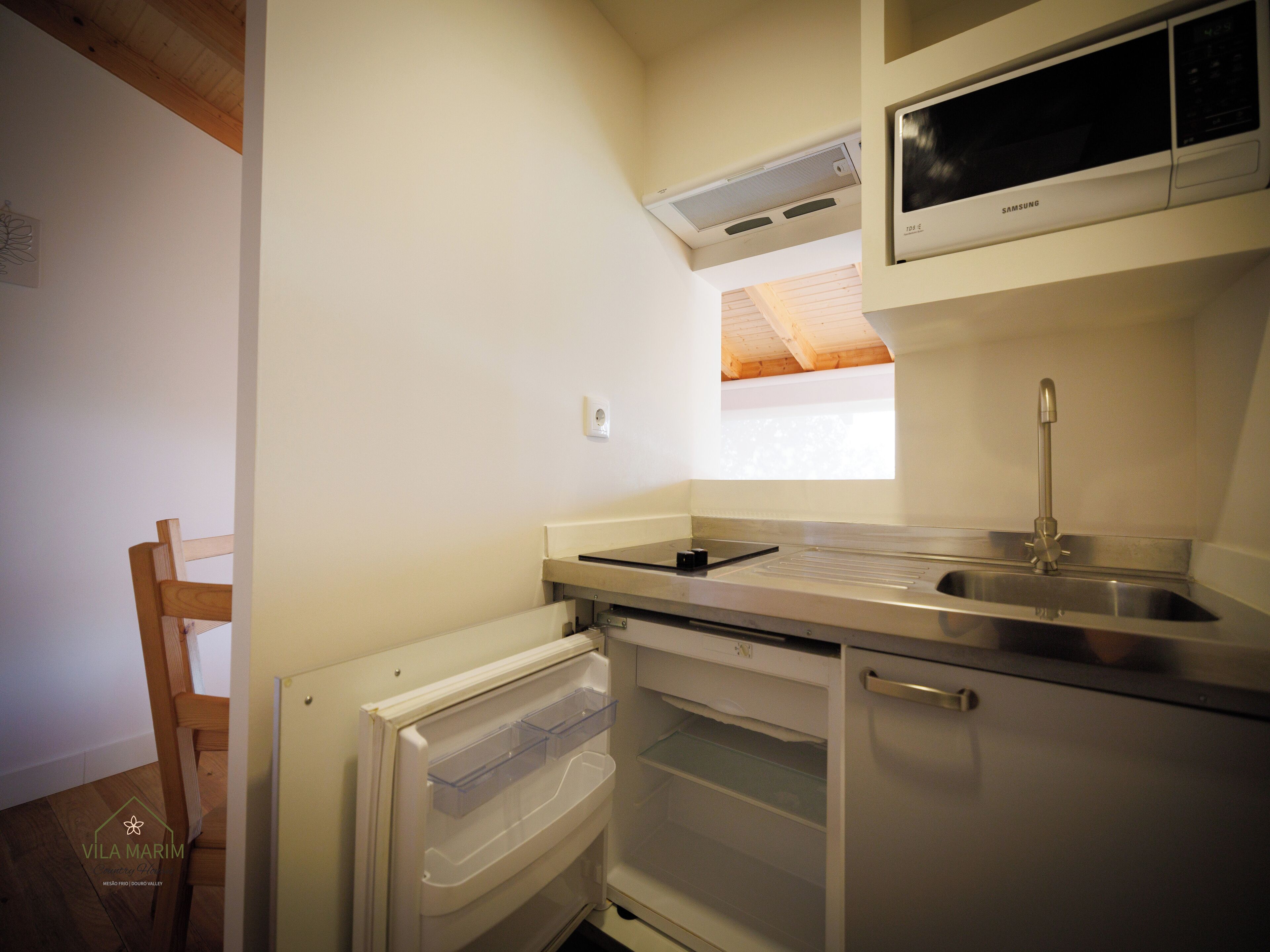 A compact kitchen with a built-in microwave, a stainless steel sink, and a wooden chair.