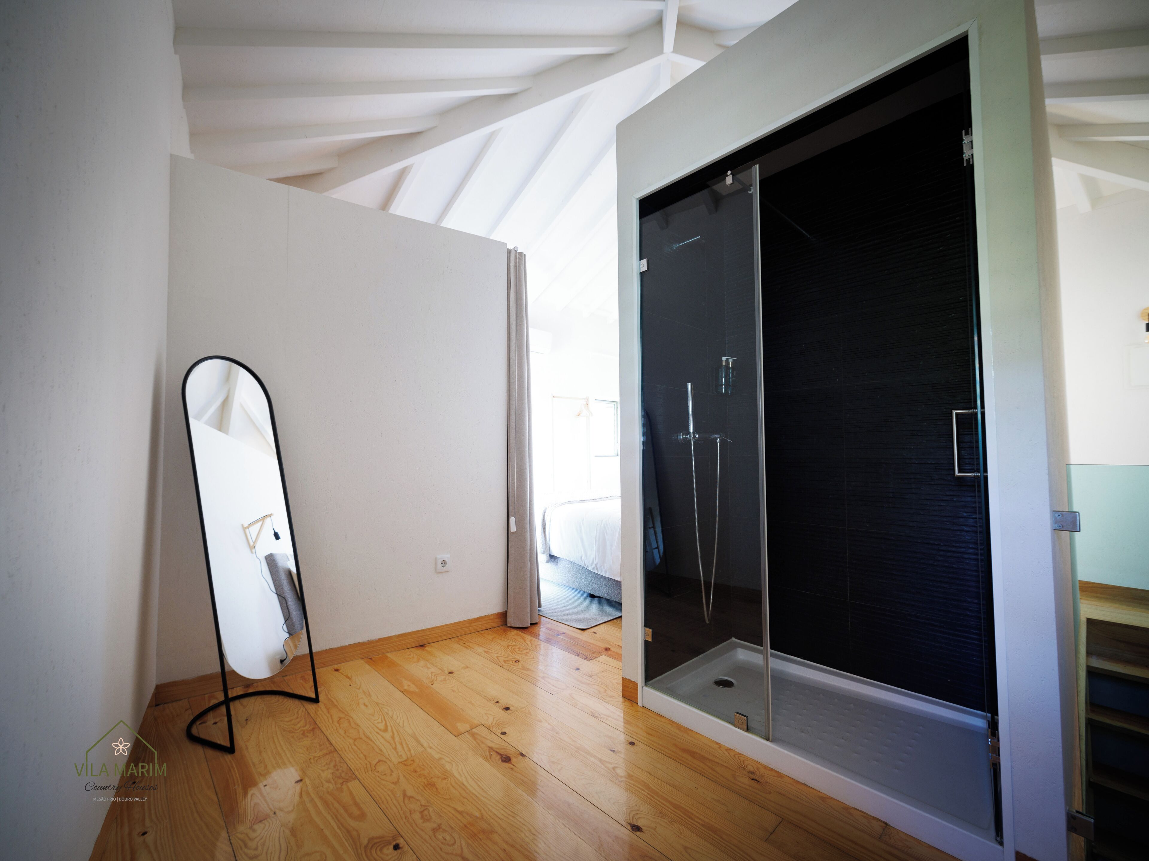 Un baño moderno con cabina de ducha de vidrio, suelo de madera y un espejo grande.