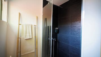 Une salle de bain dotée d’une douche à parois de verre, d’un porte-serviettes en bambou et d’un mur recouvert de carreaux foncés.
