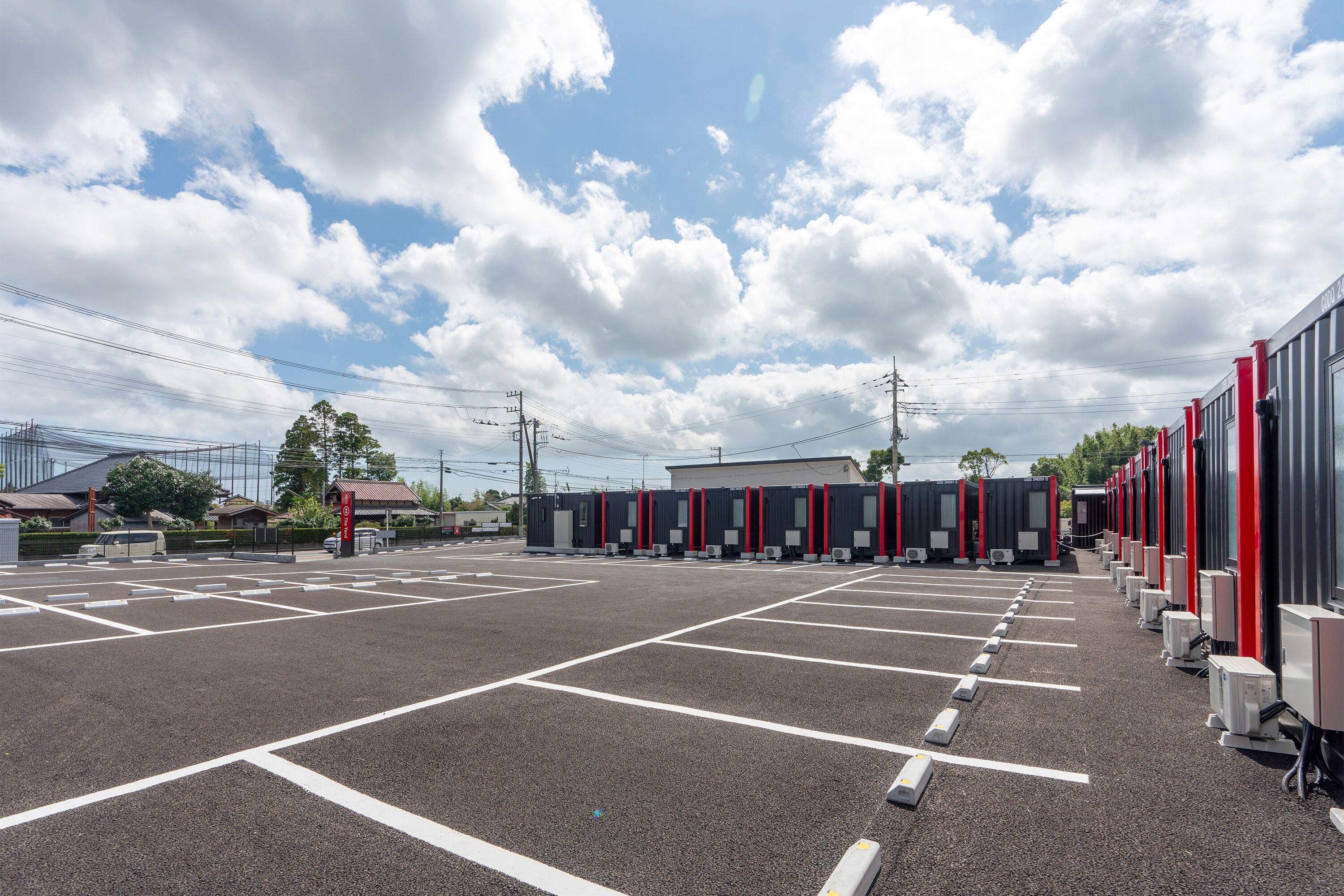 A parking lot with marked parking spaces and a row of buildings with red and black exterior walls.