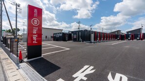 Ein Hotel mit Eingang, rotem Schild, Parkplatz und einem Gebäude im Hintergrund.