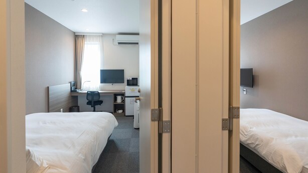 Ein Hotelzimmer mit zwei Betten, einem Schreibtisch mit Computer, einem Fernseher und einer Mikrowelle.