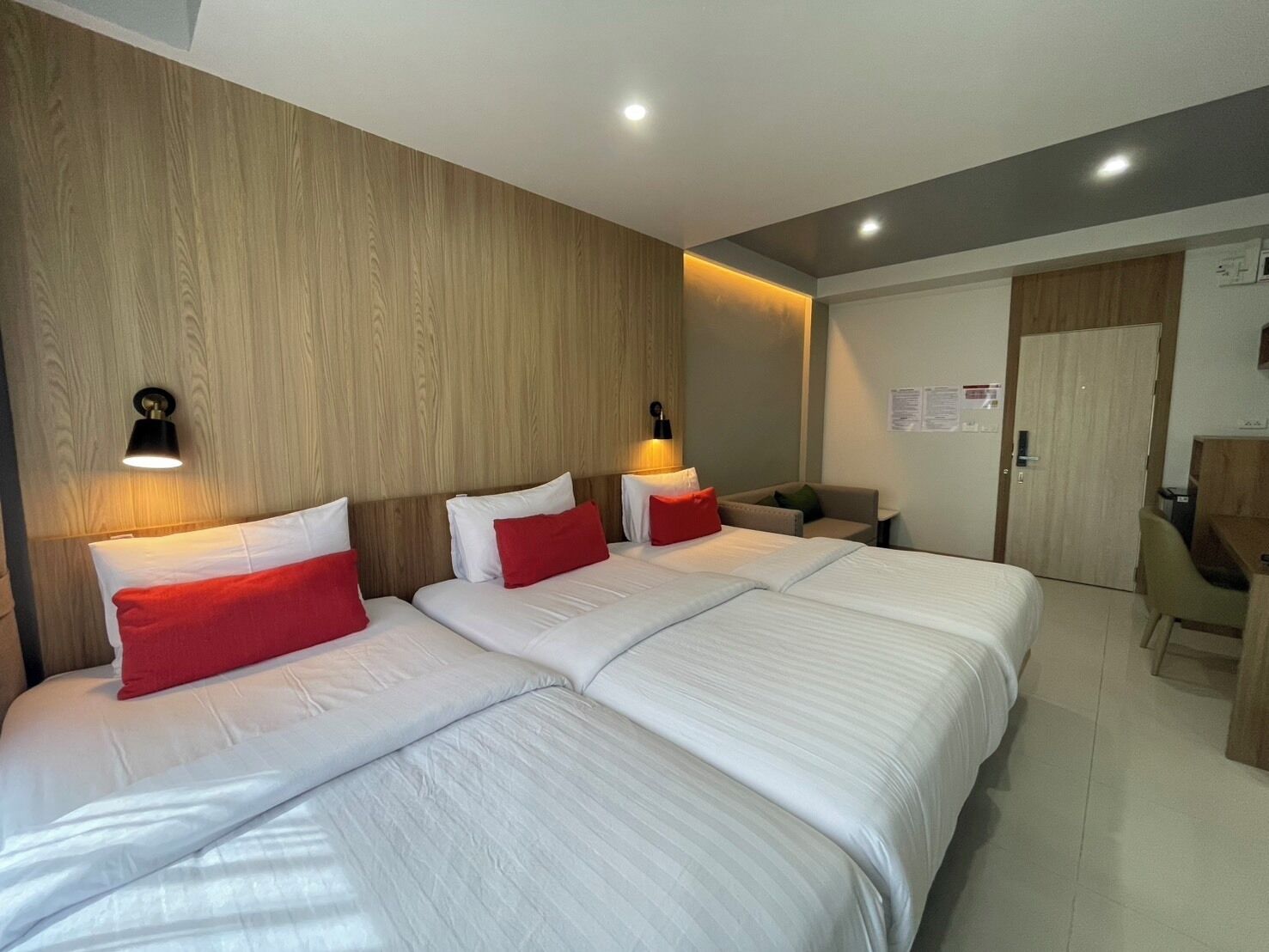 A hotel room with three beds, wooden paneling on the walls, and a desk with a chair.