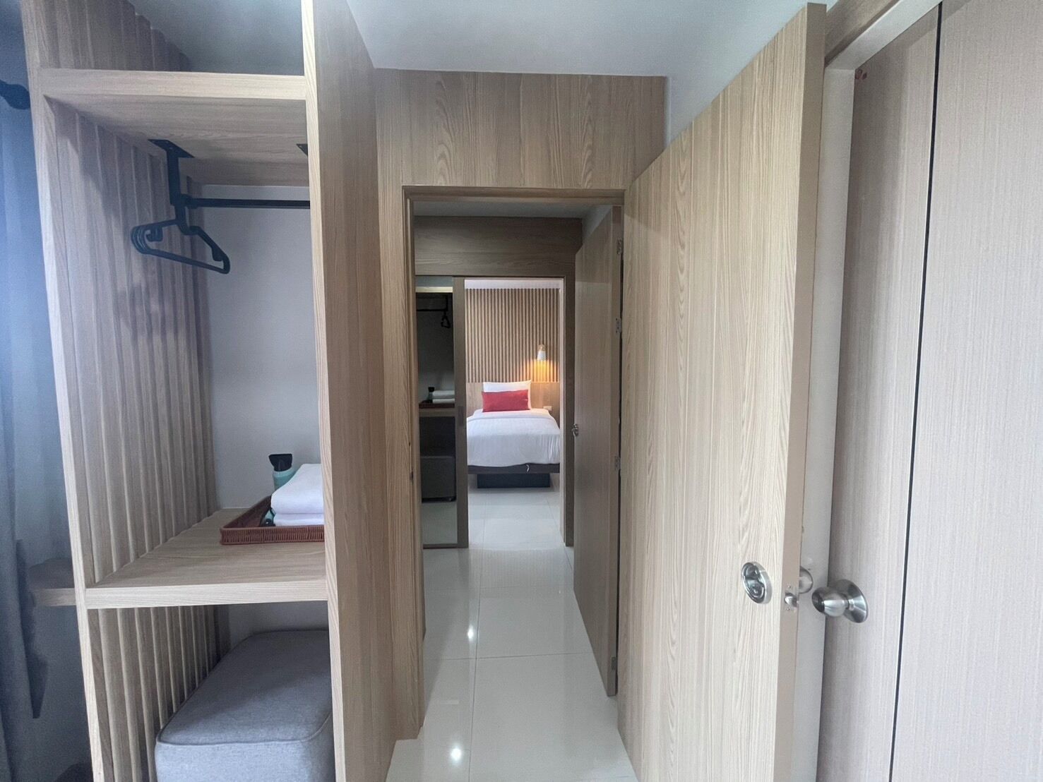 Ein modernes Hotelzimmer mit begehbarem Kleiderschrank, einem Bett mit rotem Zierkissen und einem Nachttisch mit Lampe.