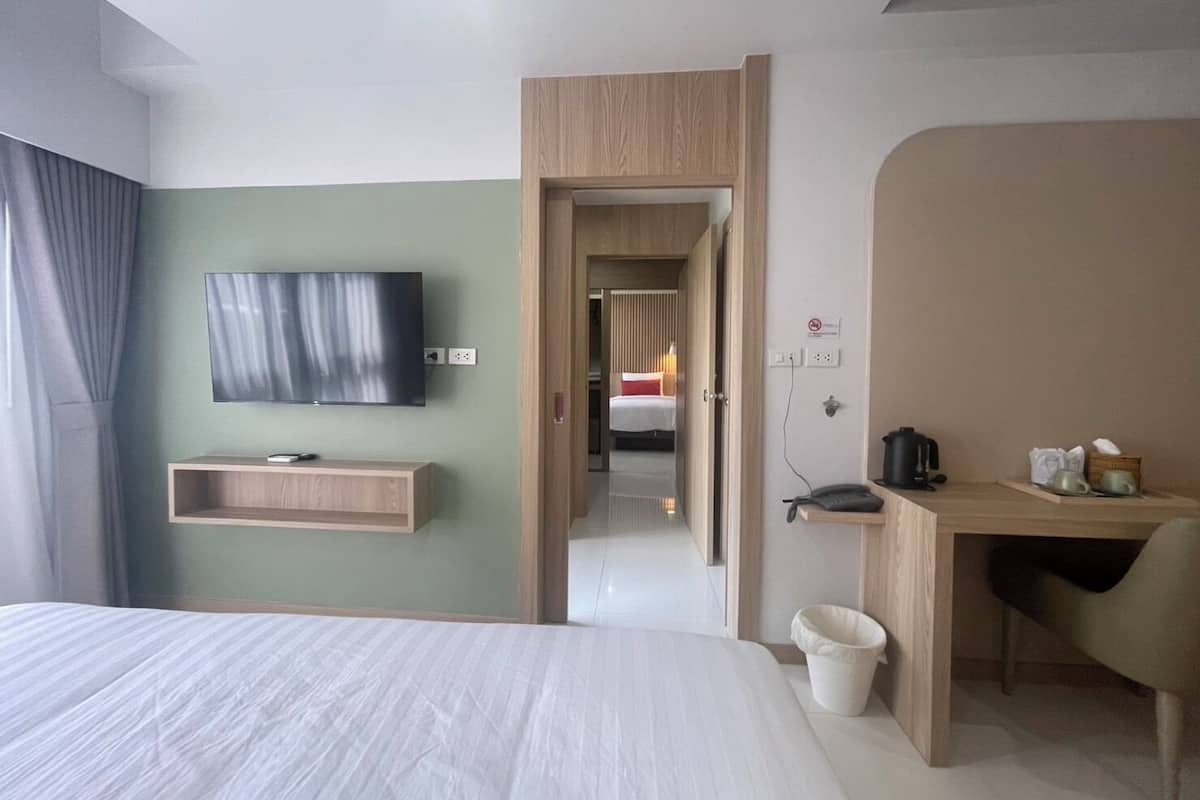 Una habitación de hotel moderna con una cama, un televisor montado en la pared, un escritorio con una silla y un cubo de basura pequeño.