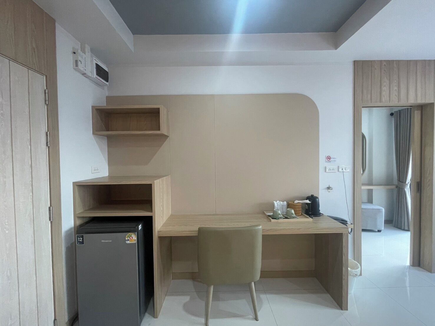 A compact kitchenette with a refrigerator, microwave, and wooden shelves.