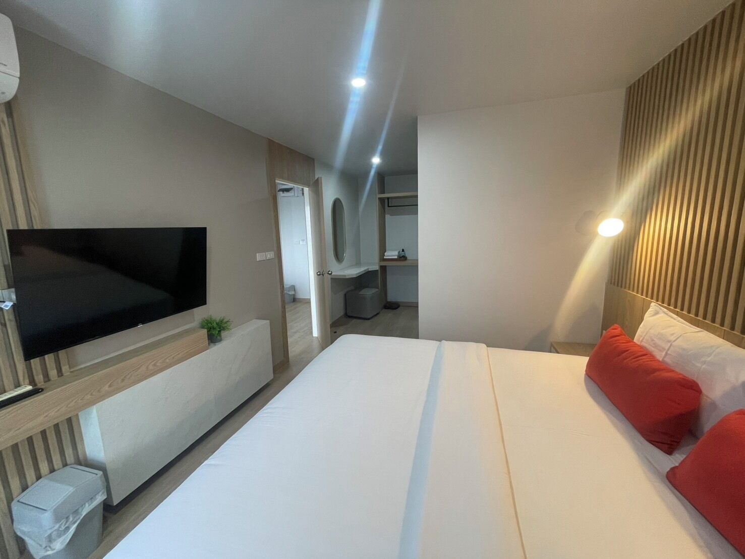 A modern hotel room with a large bed, a flat-screen TV, a small trash bin, and a mirror above the bed.